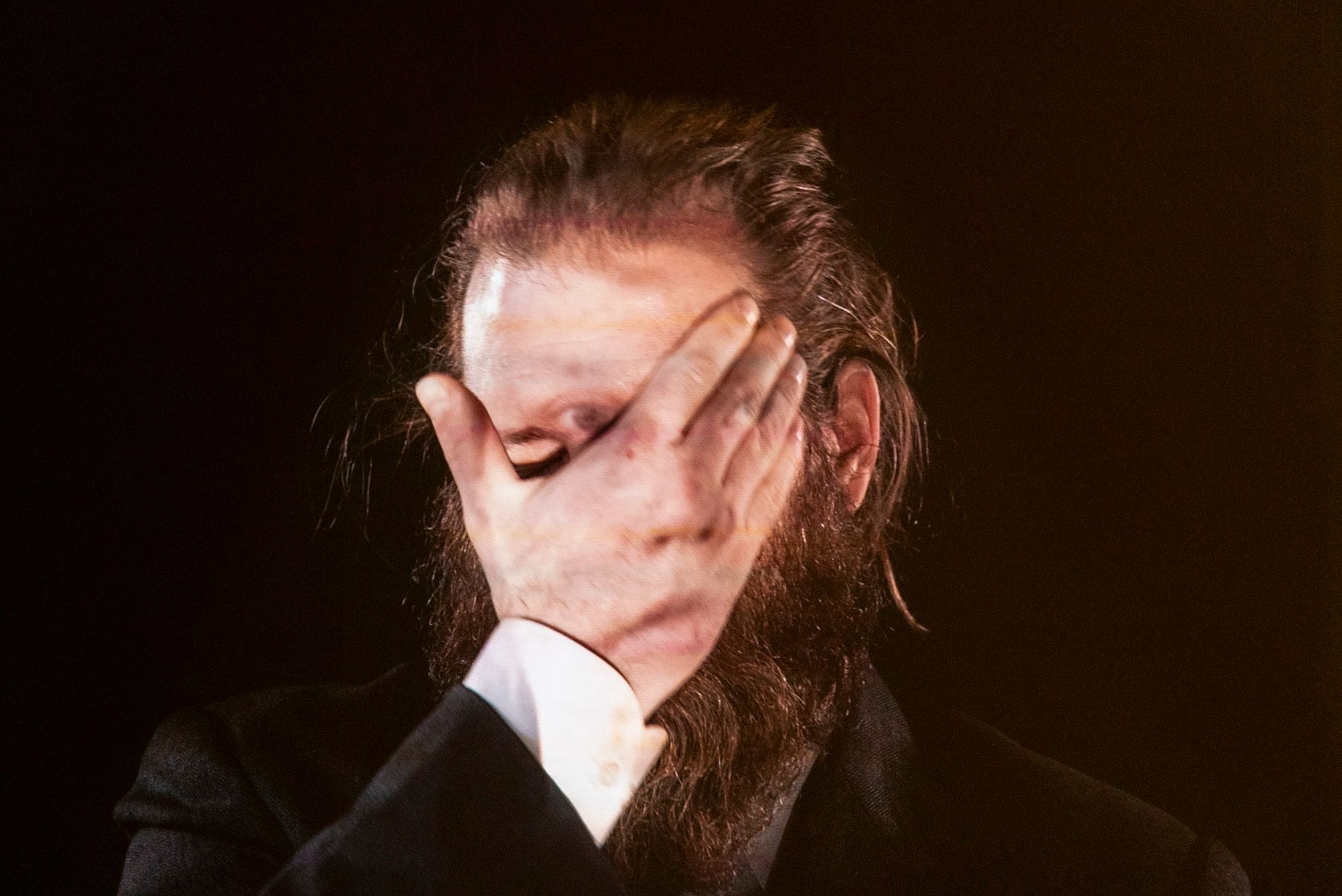 A picture of Pasi with his hand in front of his face, where onto him is projected a picture of Mammu, thus displaying her features on his hand.