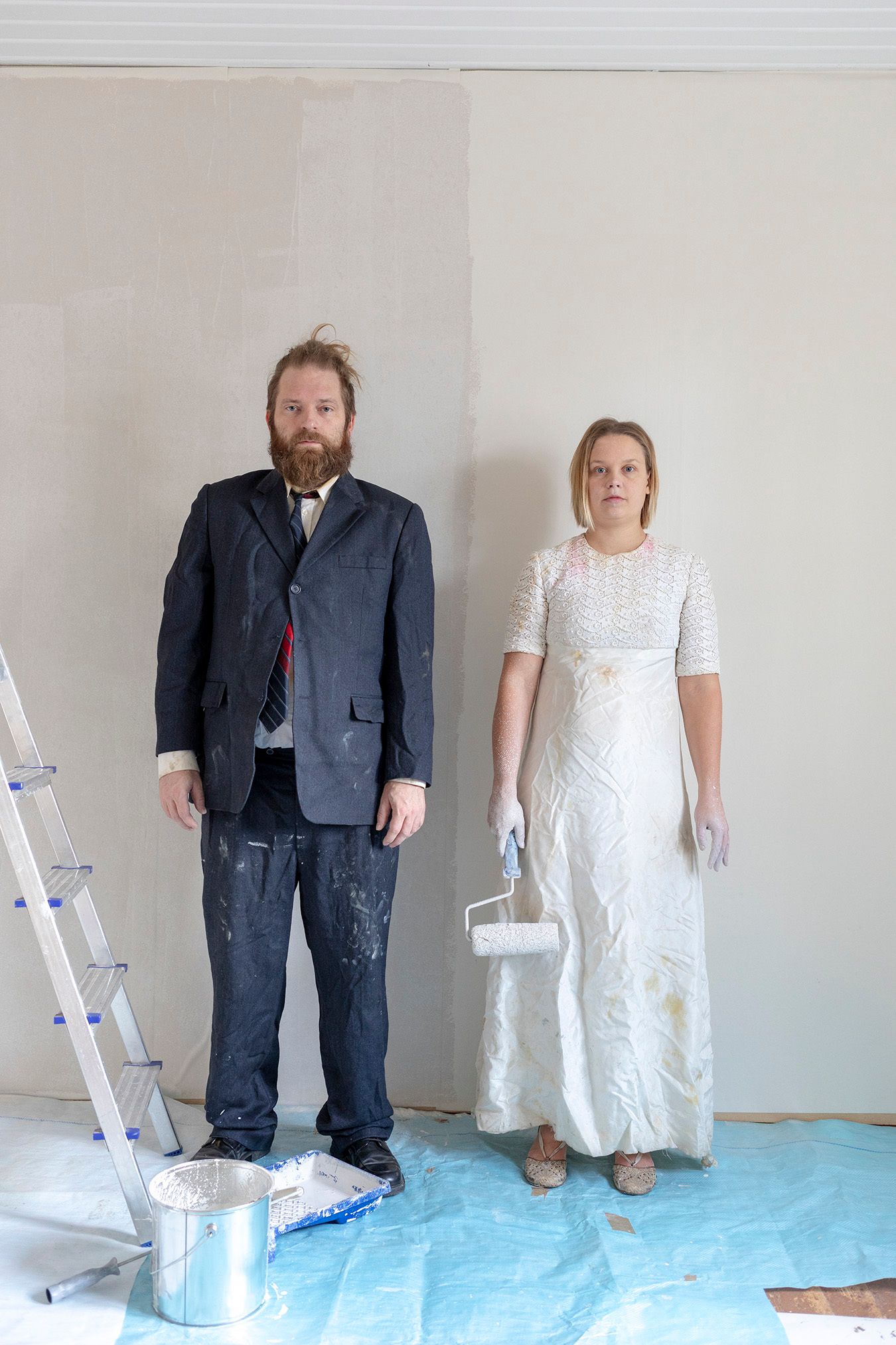 Mammu and Pasi standing in their wedding attire with neutral expressions staring at the camera.