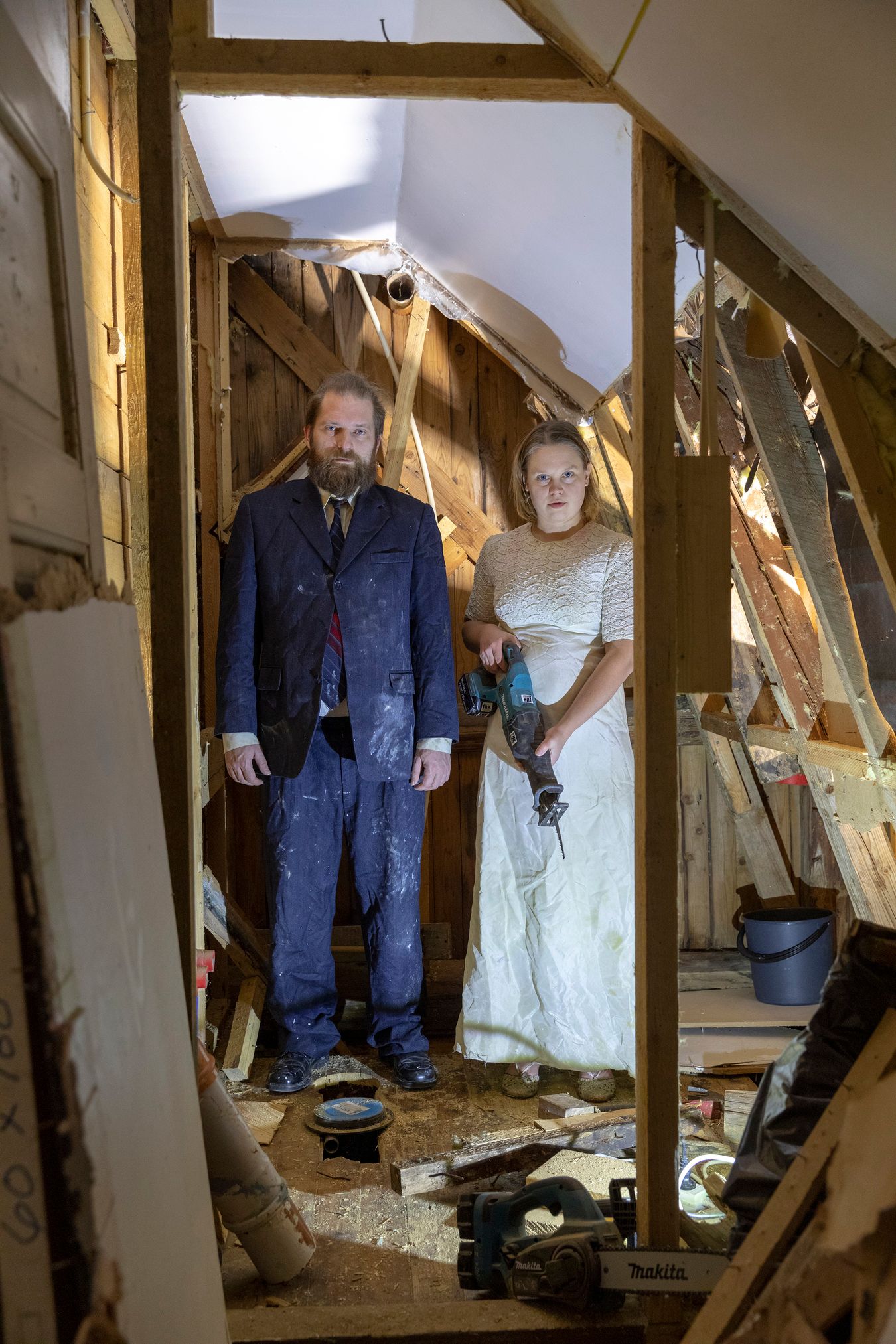 Mammu and Pasi standing in their wedding attire with neutral expressions staring at the camera.