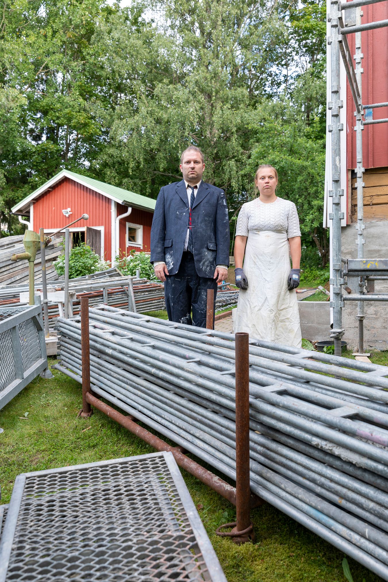 Mammu and Pasi standing in their wedding attire with neutral expressions staring at the camera.