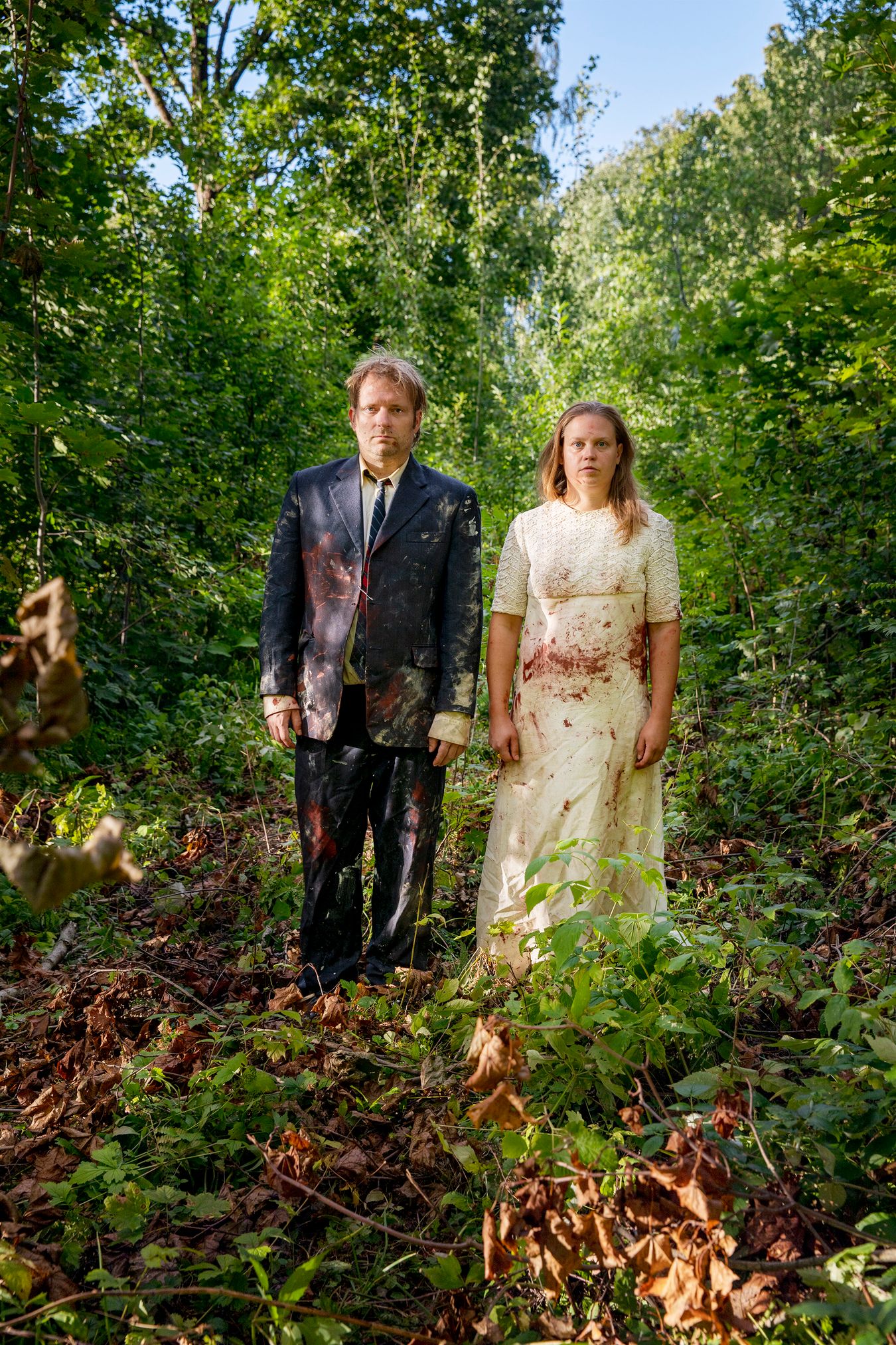 Mammu and Pasi standing in their wedding attire with neutral expressions staring at the camera.