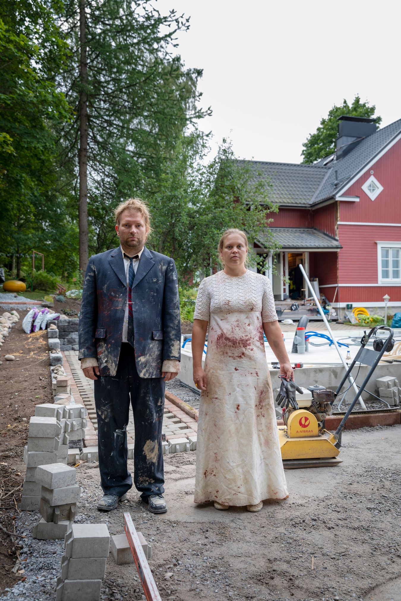 Mammu and Pasi standing in their wedding attire with neutral expressions staring at the camera.