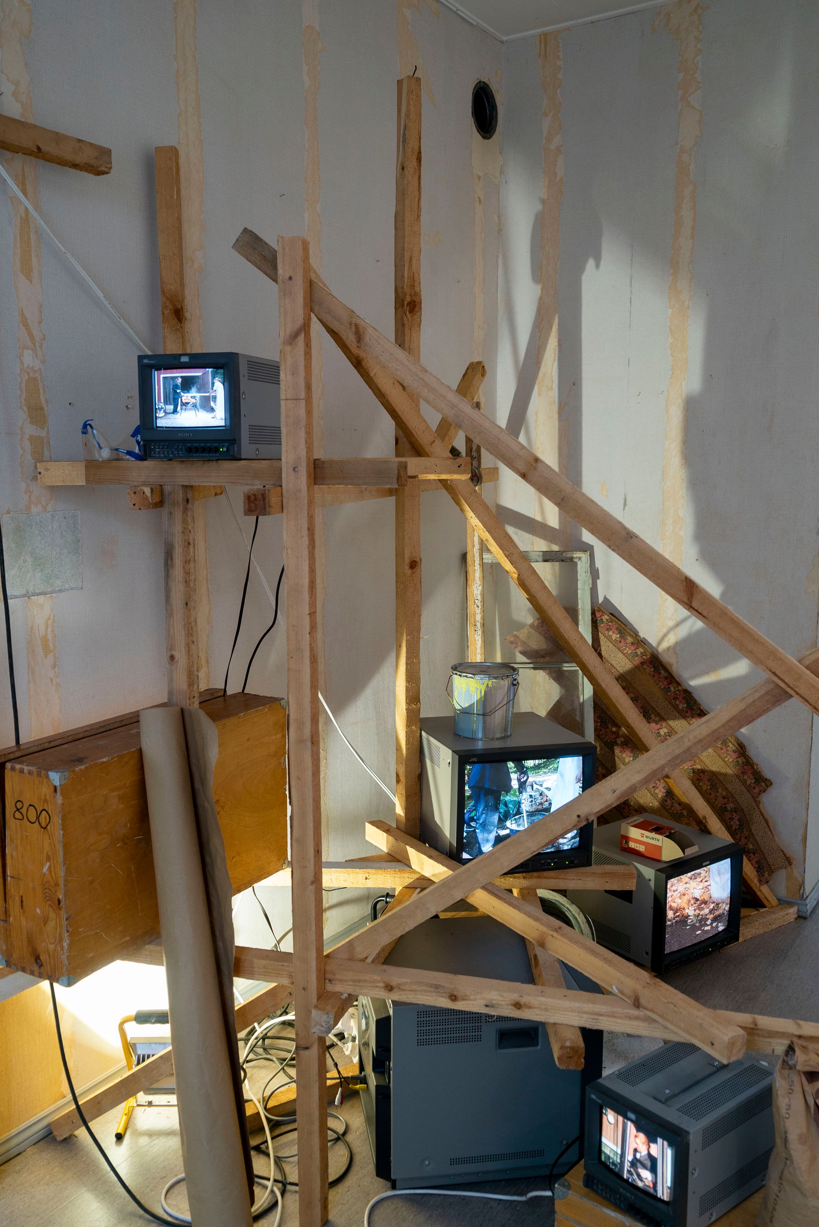 Installation of videos on CRT monitors on wooden scaffolding next to assorted construction equipment.