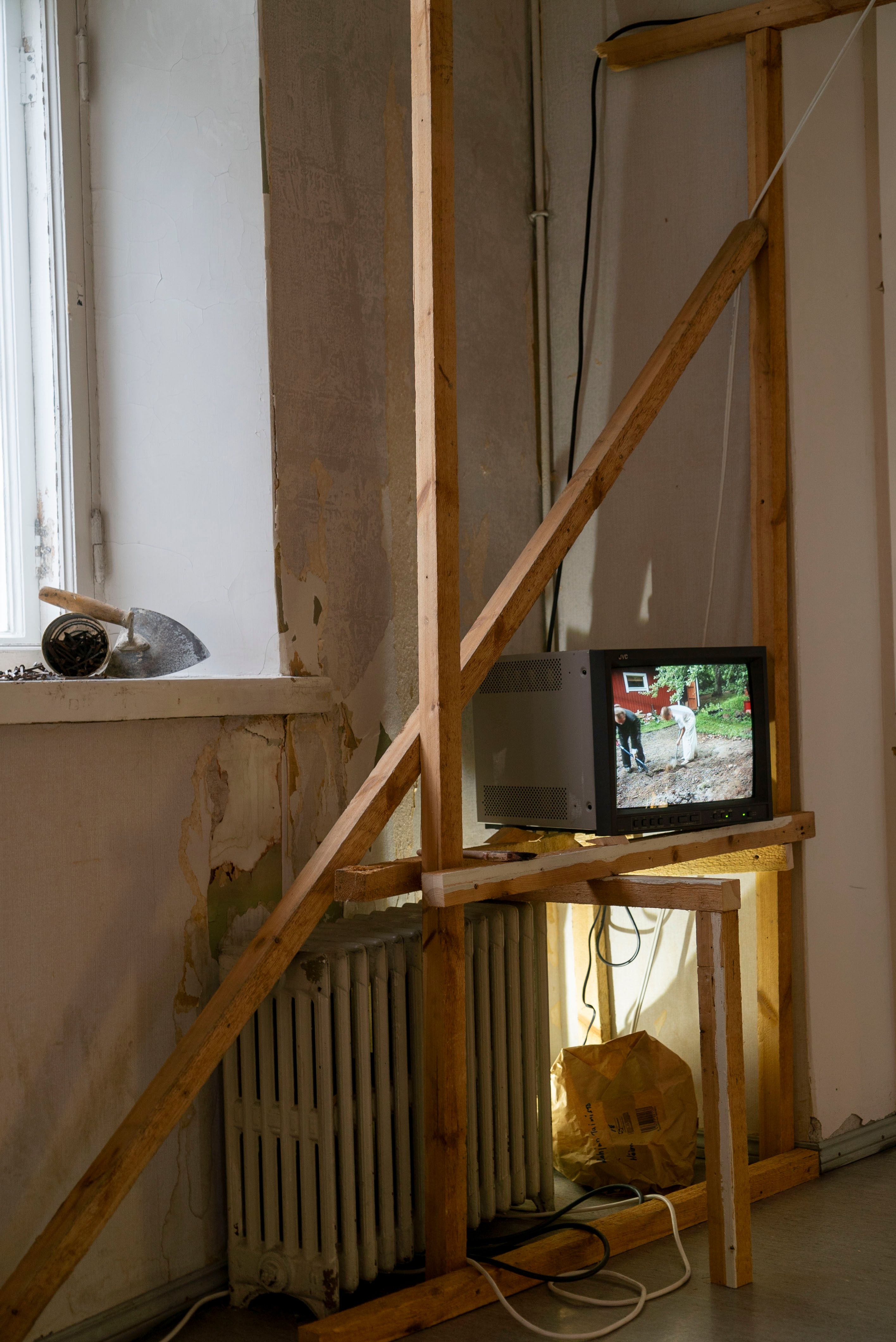 Installation of videos on CRT monitors on wooden scaffolding next to assorted construction equipment.