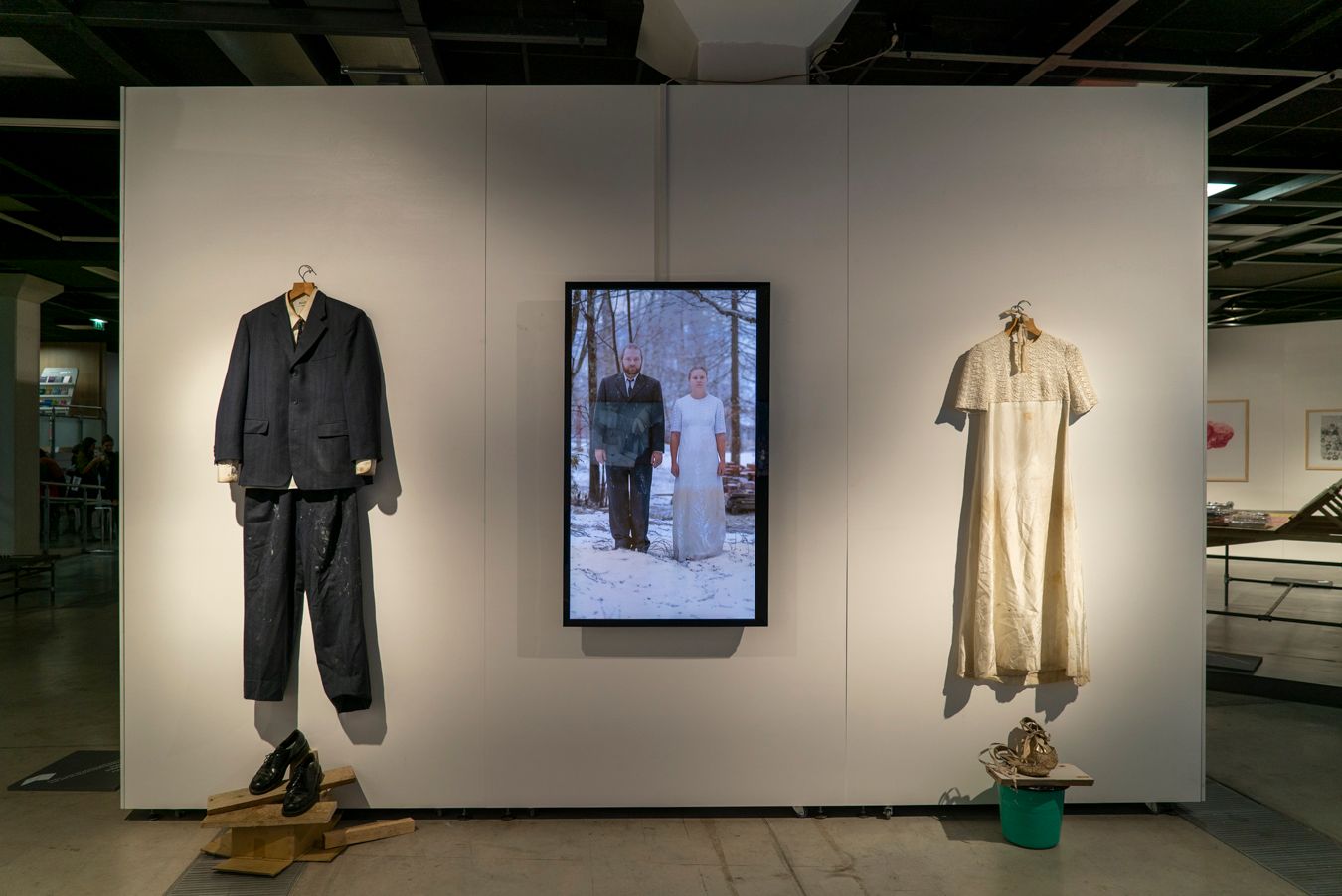 Mammu's and Pasi's wedding attire hanging from a wall, next to a video of them standing in snow in the same clothing.