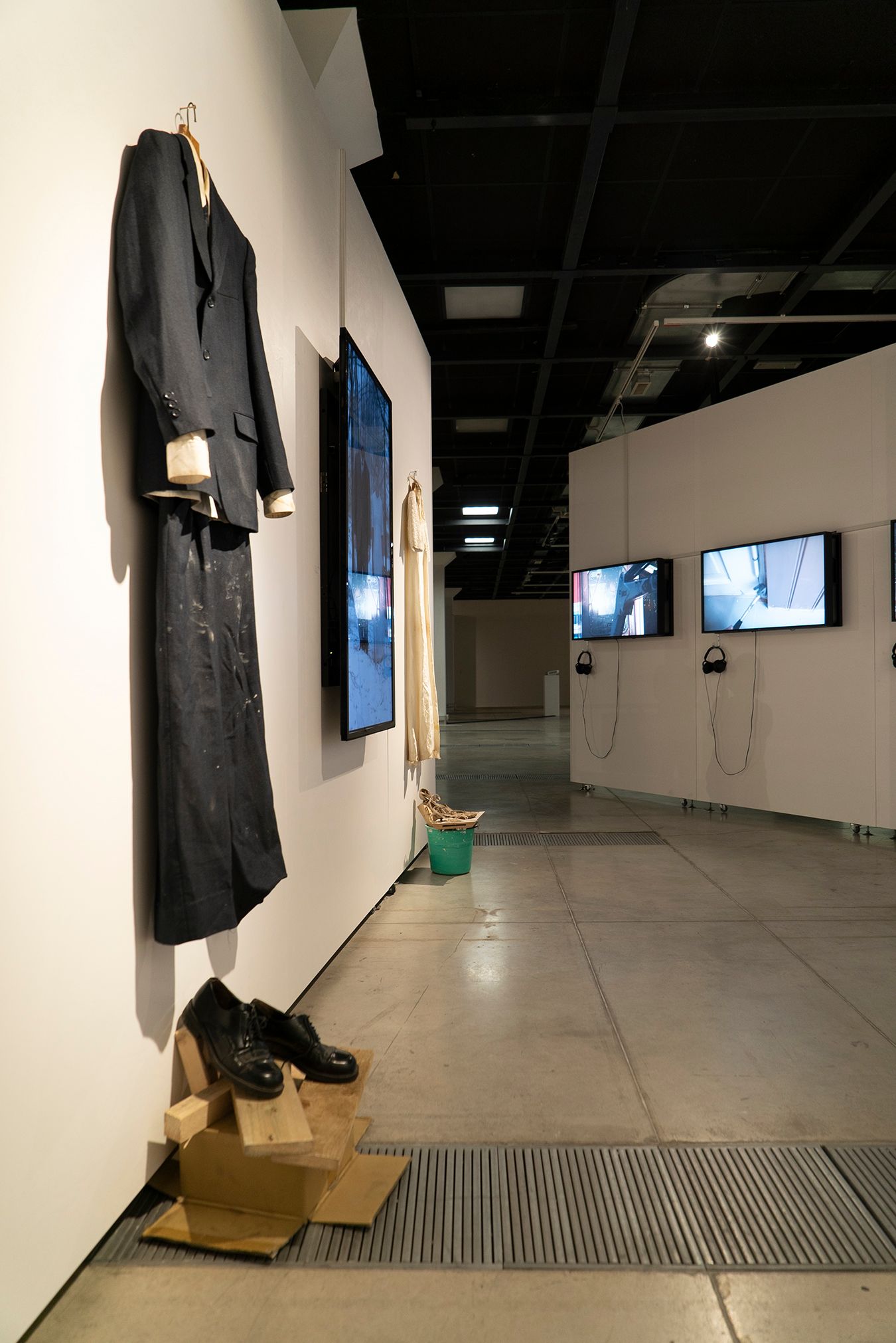 General view from an exhibition, showcasing Mammu's and Pasi's attire, some photographs, and some videos.